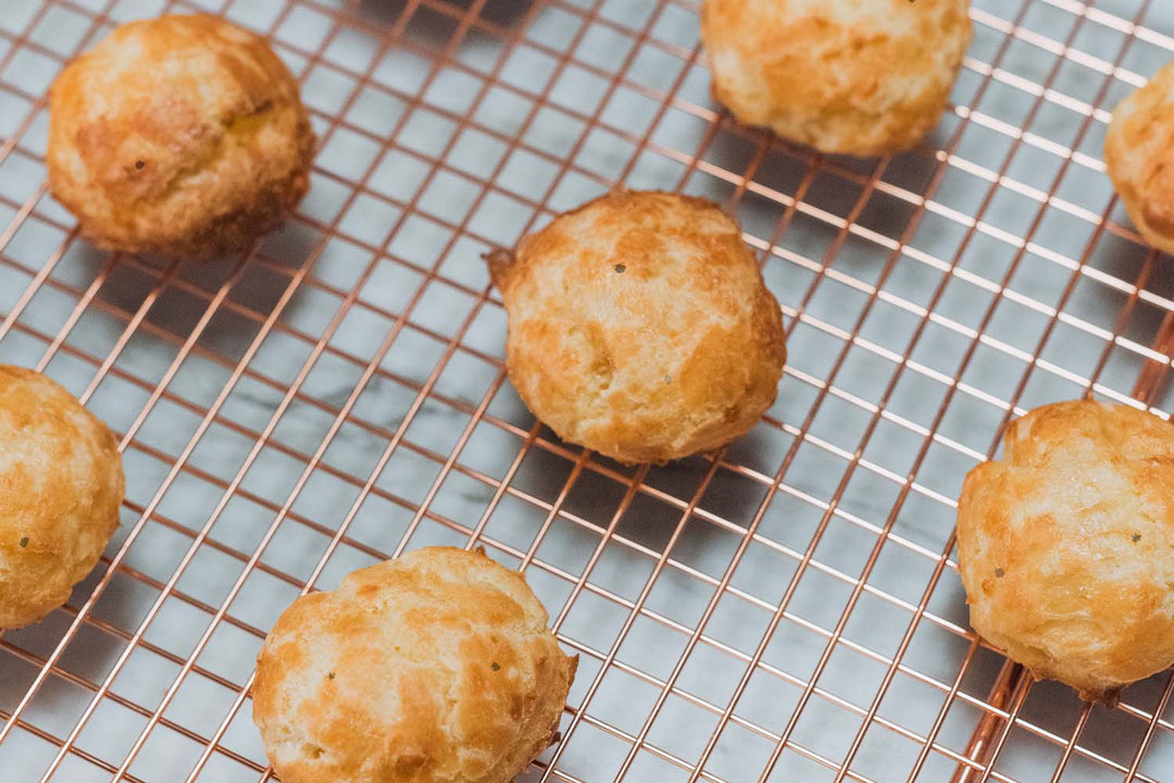 Closeup of baked gougères on a baking sheet. Some black speckles from the black pepper from the cacio e pepe flavor